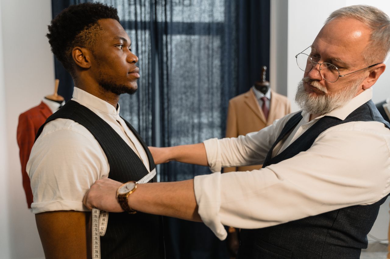 our-story Professional tailor takes measurements for a bespoke suit fitting in a tailoring workshop.